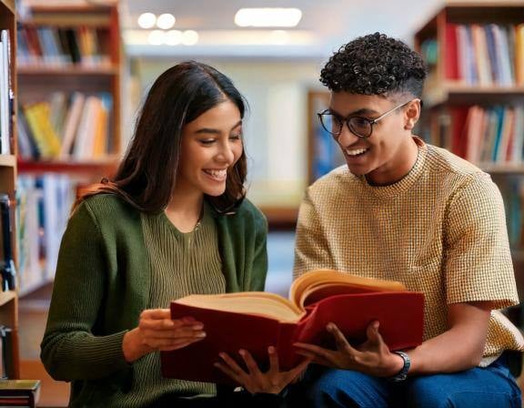 Firefly Dos estudiantes universitarios, mirando un libro en la mano, sentados dentro de una bibliote